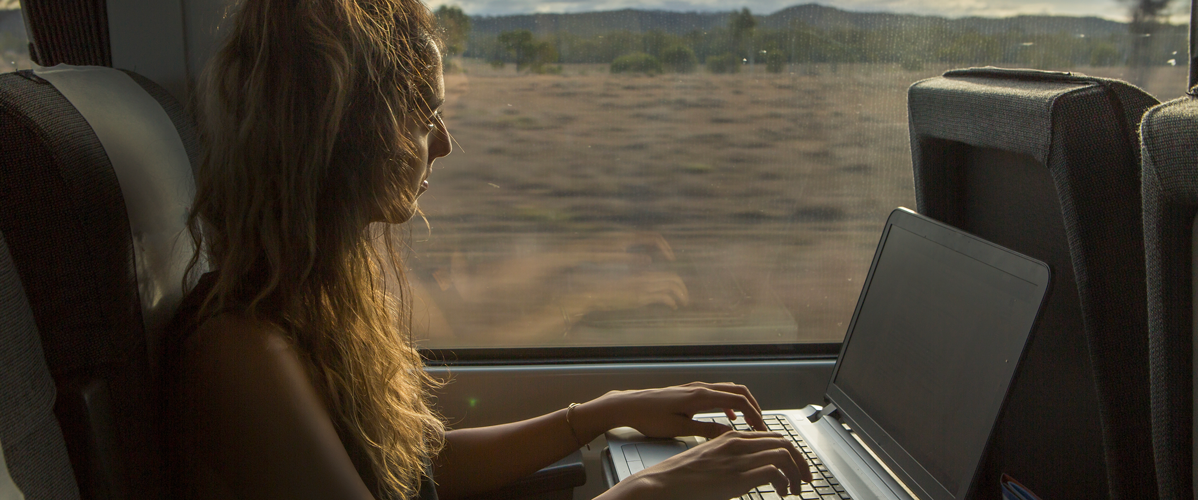 A young woman watches a live video on her computer on the train