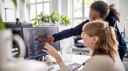 Two women discuss over code displayed on the computer screen