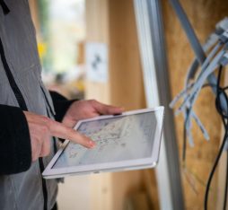 GettyImages - Main d'homme en gilet gris consulte une tablette sur un chantier, avec des câbles visibles en arrière-plan.