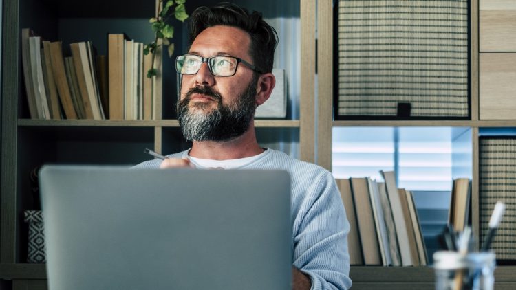 Getty Images - Thoughtful businessman with laptop sitting at desk in home office