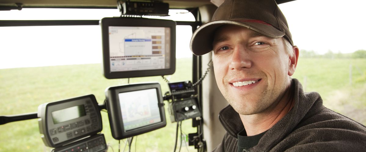 An operator is inside a modern tractor, surrounded by control screens displaying agricultural data.