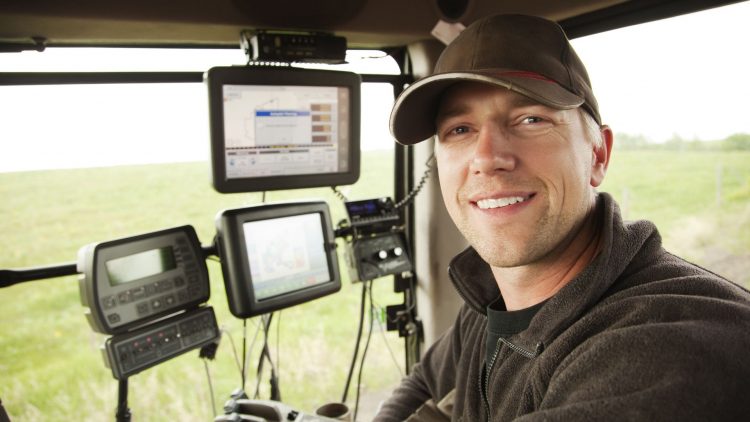 An operator is inside a modern tractor, surrounded by control screens displaying agricultural data.