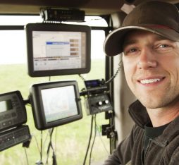 An operator is inside a modern tractor, surrounded by control screens displaying agricultural data.