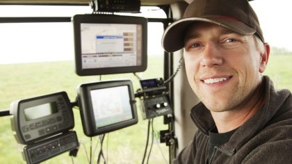 An operator is inside a modern tractor, surrounded by control screens displaying agricultural data.