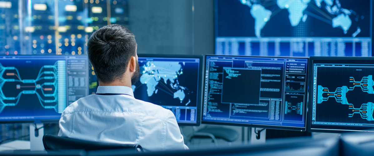 A man at his desk checks datasets on multiple screens