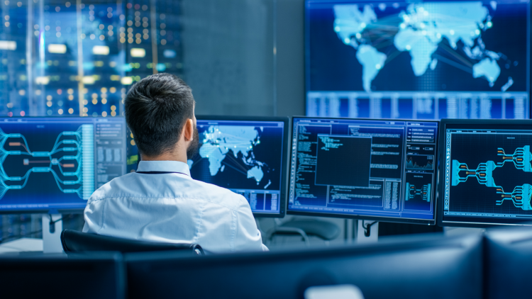 A man at his desk checks datasets on multiple screens