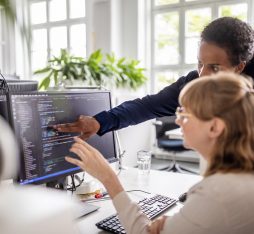 Two women discuss over code displayed on the computer screen
