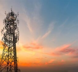 Une tour de télécommunications métallique équipée de nombreuses antennes, sur un ciel coloré par un coucher de soleil aux teintes orange, rose et bleues.