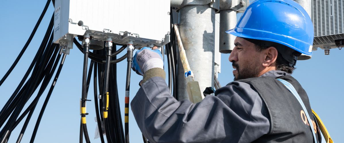 Technicien équipé d’un casque de sécurité installant et connectant des câbles sur un équipement télécom en hauteur.
