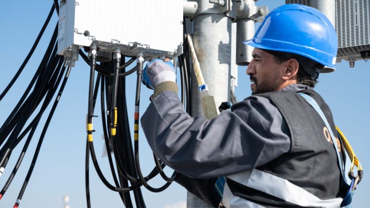 Technicien équipé d’un casque de sécurité installant et connectant des câbles sur un équipement télécom en hauteur.
