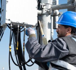 Technicien équipé d’un casque de sécurité installant et connectant des câbles sur un équipement télécom en hauteur.
