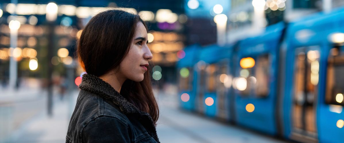 Young woman waiting for a tram in an urban environment at dusk.