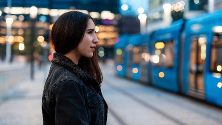 Young woman waiting for a tram in an urban environment at dusk.