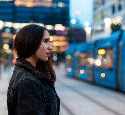 Jeune femme attendant un tramway dans un environnement urbain en début de soirée.