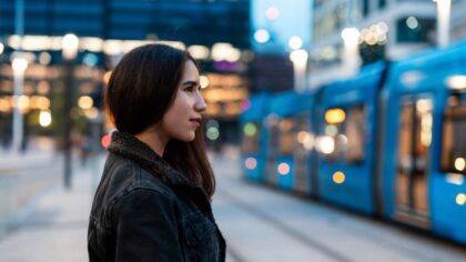 Jeune femme attendant un tramway dans un environnement urbain en début de soirée.