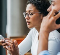 Two people using smartphones: one looking at the screen while the other is making a phone call.