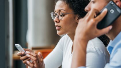 Deux personnes utilisent un smartphone : l’une consulte son écran tandis que l’autre passe un appel téléphonique.